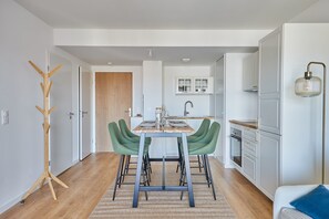 Una cucina moderna con mobili bianchi, forno integrato e zona pranzo con tavolo in legno e sedie verdi.