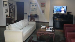Un saló amb un sofà blanc, un butaca vermella, una taula de centre i una televisió que mostra un canal d'informatius.