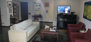 Ein Wohnzimmer mit einem weißen Sofa, einem roten Sessel, einem Couchtisch und einem Fernseher, der einen Nachrichtensender zeigt.