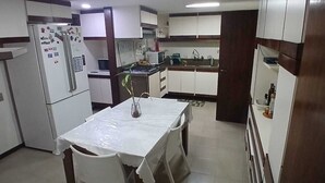 Una cuina compacta amb armaris blancs, un refrigerador, un microones i una taula de menjador amb cadires.
