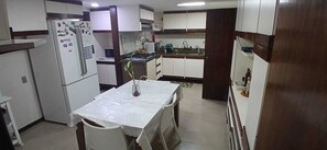 Eine kompakte Küche mit weißen Schränken, einem Kühlschrank, einer Mikrowelle und einem Esstisch mit Stühlen.