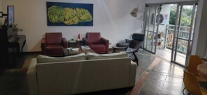 A living room with a sofa, two armchairs, a coffee table, and a television. There is a large painting of bananas on the wall. - Spacious Leblon. Excellent location. (Rio de Janeiro)