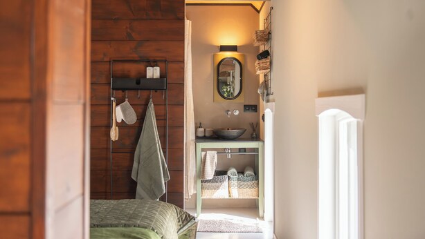 A compact bedroom with a bed, a bedside table, and a small bathroom with a sink and mirror.