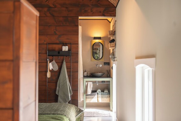 A compact bedroom with a bed, a bedside table, and a small bathroom with a sink and mirror.