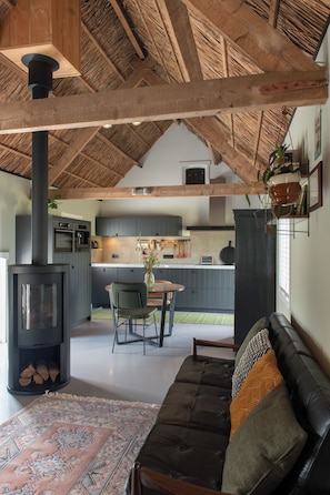 Un interior acogedor con techo de paja, un sofá negro, una mesa de comedor con sillas y una zona de cocina con armarios grises.