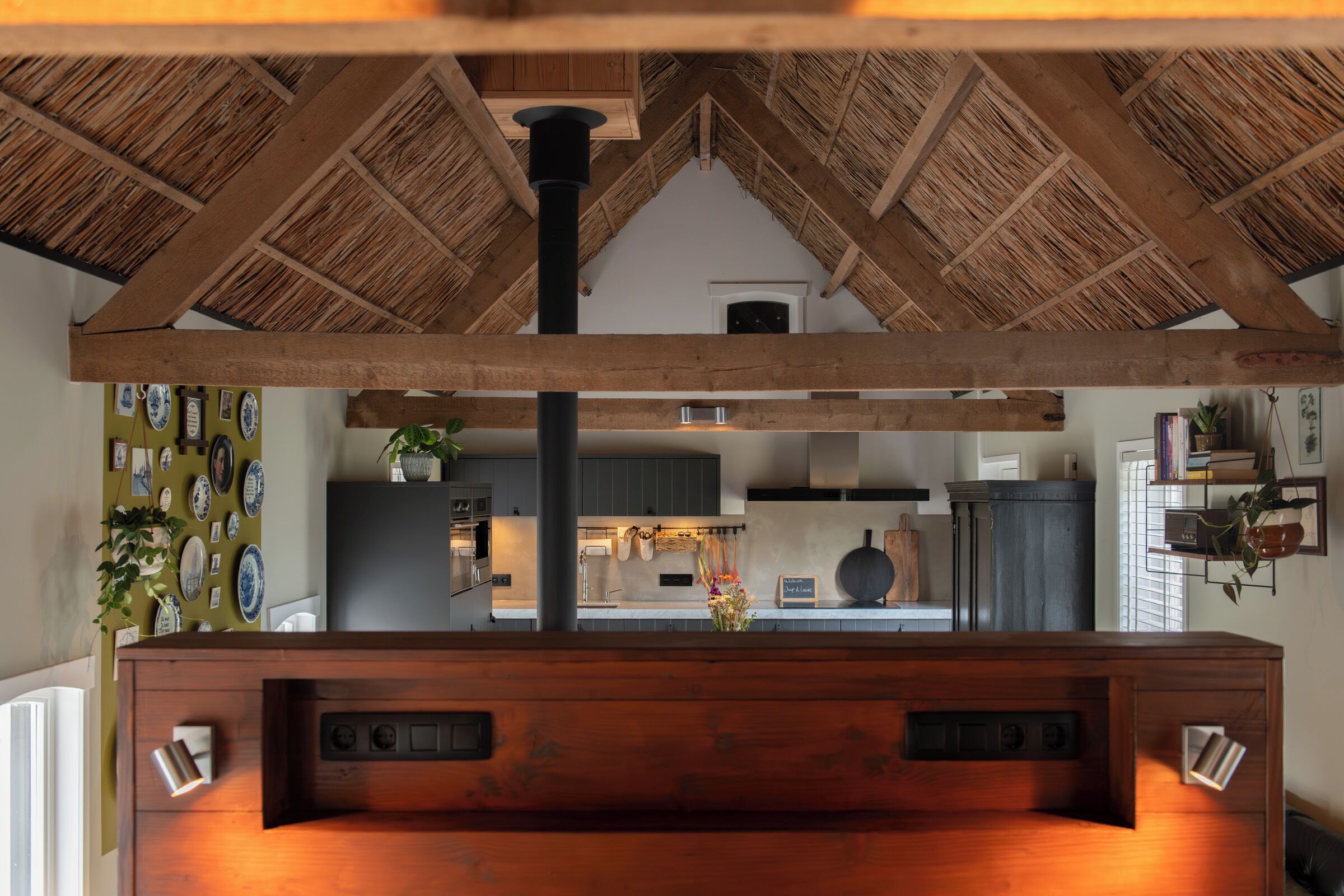 Una cocina con techo de madera, un tubo negro central y vista al área de comedor.