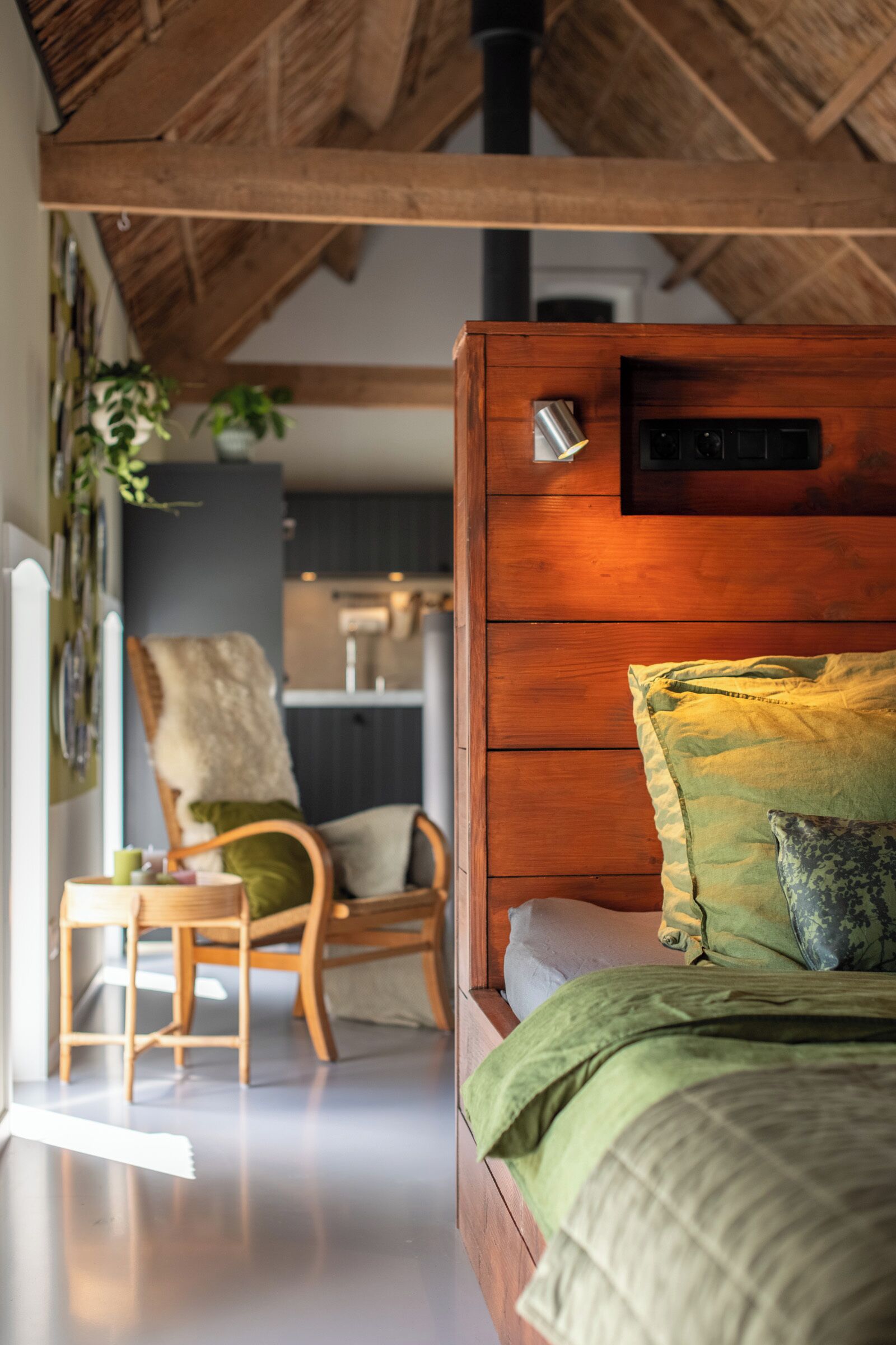 Un dormitorio con cabecera de madera, cama con ropa de cama verde, una silla y un escritorio.