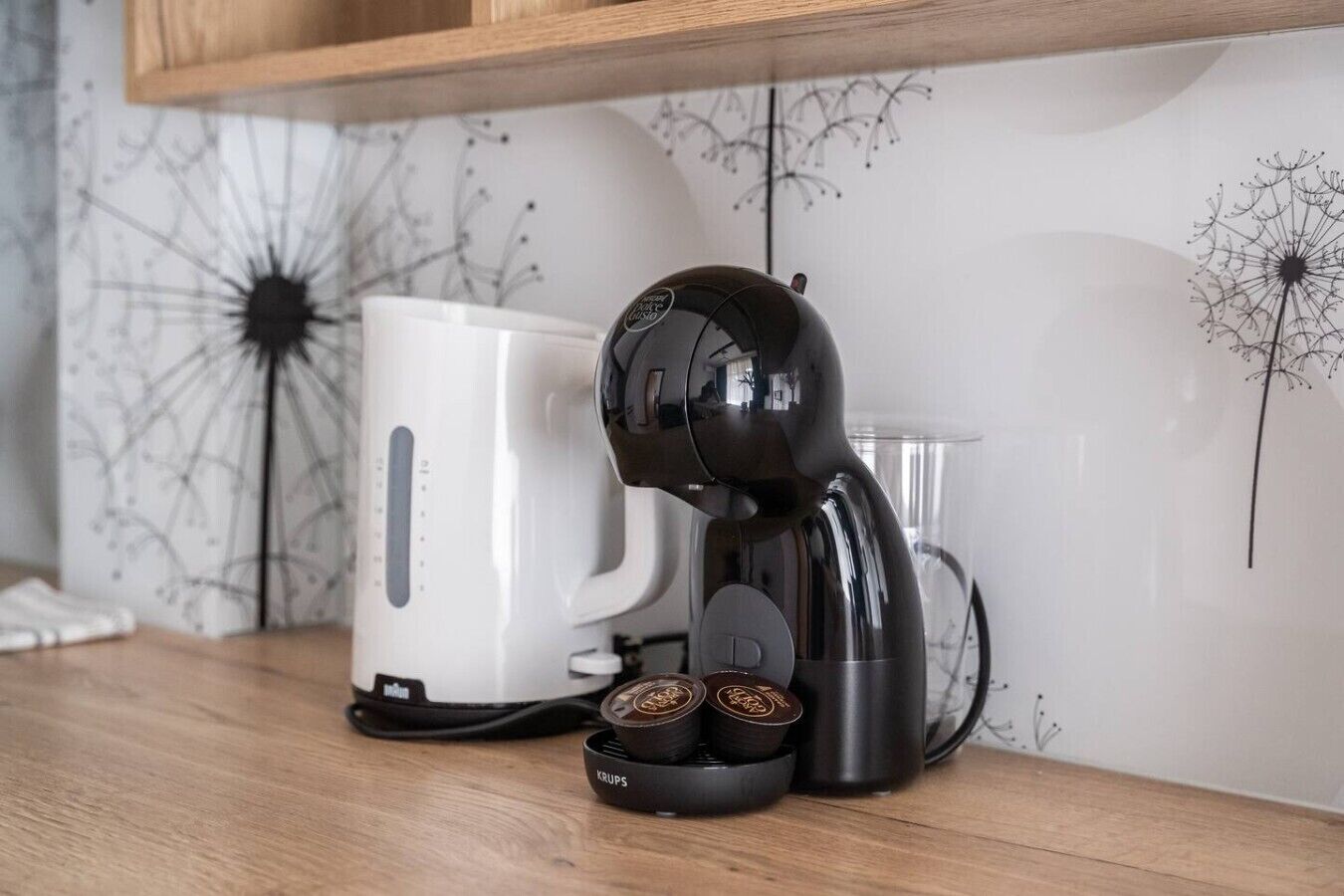 Eine Kaffeemaschine mit Wasserbehälter und zwei Kaffeekapseln auf einer Holzauskleidung.