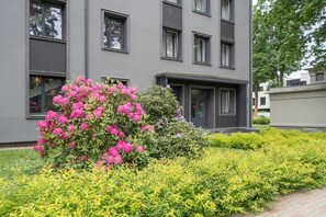 Un edificio moderno con techo plano, grandes ventanales y un jardín cuidado con arbustos florecientes.