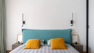 Ein Schlafzimmer mit einem türkisfarbenen Kopfteil, zwei Nachttischen mit Lampen sowie einem Bett mit einem gemusterten Bettbezug und zwei Kissen.