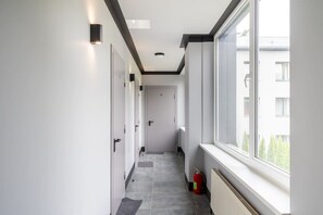 Un couloir avec une fenêtre sur la droite, une porte au fond et un extincteur près de la fenêtre.