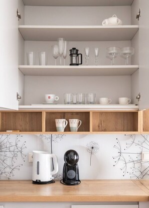 Une cuisine avec des meubles blancs, une machine à café et une bouilloire posées sur le plan de travail.
