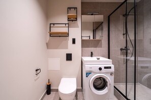 Une salle de bain moderne équipée de toilettes, d’un lave-linge et d’une douche à parois en verre.