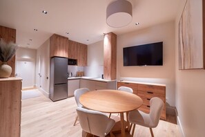 A modern kitchen with a built-in refrigerator, wooden cabinets, a dining table with chairs, and a flat-screen TV mounted on the wall. - Elegant 2-Bedroom 50m² Apartment | Old Town Riga (Riga)