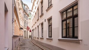 Una estrecha calle empedrada flanqueada por edificios con grandes ventanales y una bandera.