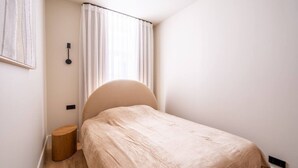 Un dormitorio pequeño y ordenado con una cama individual, una mesita de noche y una lámpara fijada a la pared.