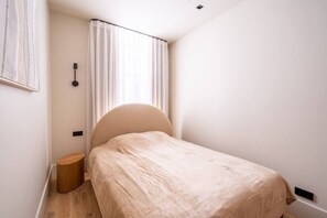 Ein kleines, ordentlich eingerichtetes Schlafzimmer mit einem Einzelbett, einem Nachttisch und einer Wandleuchte.