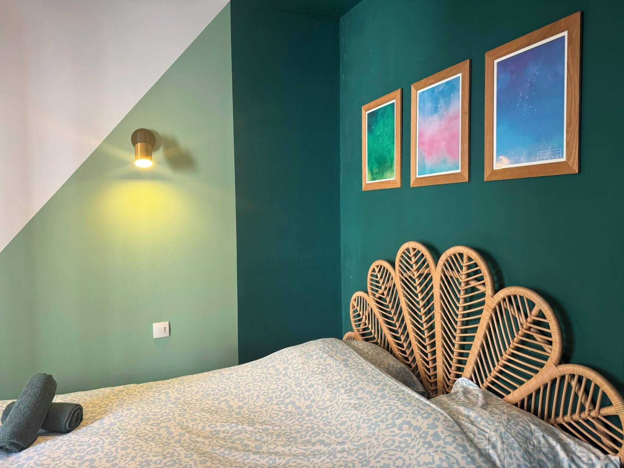 Ein Schlafzimmer mit schrägem Dach, einem Bett mit gemustertem Überwurf, einer Wandleuchte und drei gerahmten Bildern.