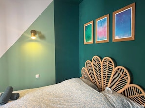 Un dormitorio con techo inclinado, una cama con colcha estampada, una lámpara fijada a la pared y tres cuadros enmarcados.