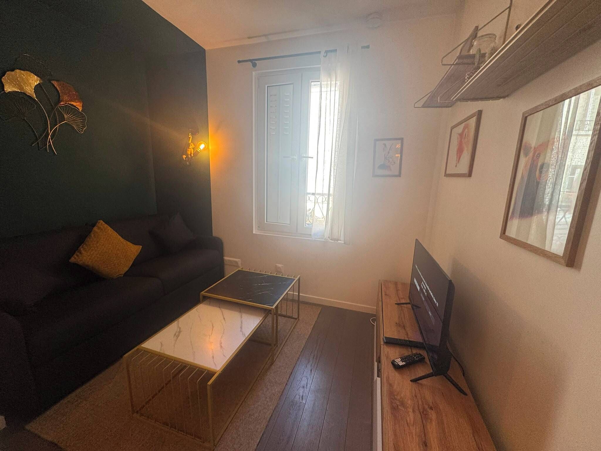 Een woonkamer met een bank, een salontafel, een televisie op een houten meubel en een raam met gordijnen.