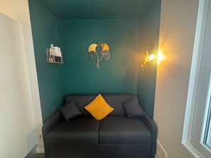 Una habitación con paredes color turquesa, un sofá negro con un cojín amarillo y adornos en la pared que incluyen una estatua de Buda y motivos de hojas.