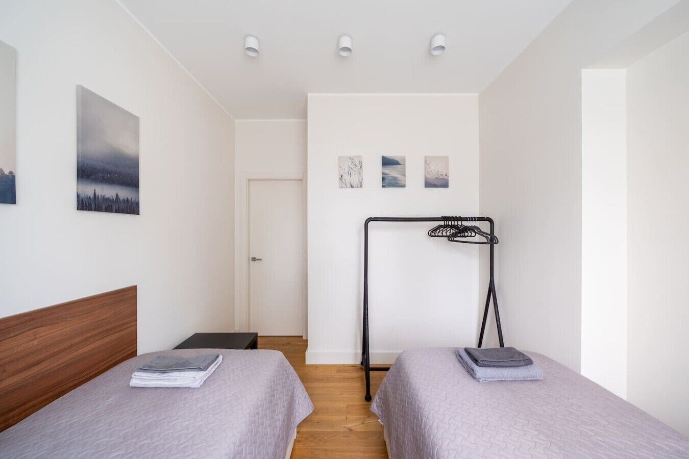 A hotel room with two single beds, a wooden headboard, a black metal drying rack, and a white door.