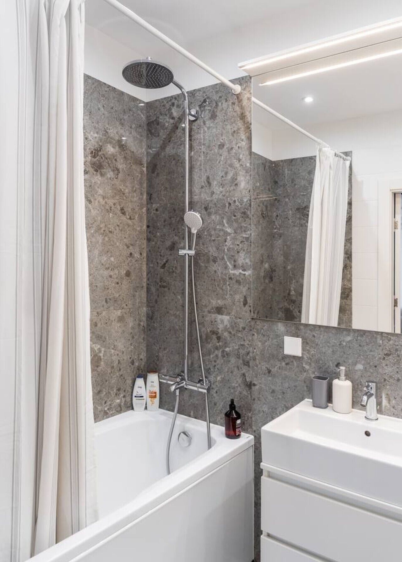 A modern bathroom with a bathtub, shower, and a large mirror.