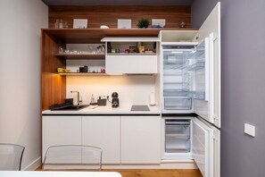 A compact kitchen with a built-in refrigerator, a coffee machine, and a small dining area with a chair.