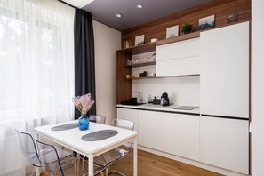 Una cocina moderna con armarios blancos, encimera negra y una zona de comedor con mesa y sillas blancas.