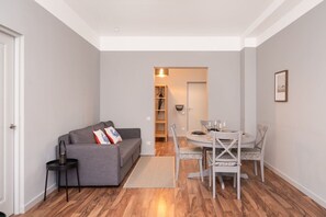 Ein modernes Wohnzimmer mit einem grauen Sofa, einem Esstisch mit Stühlen und einem Holzboden.