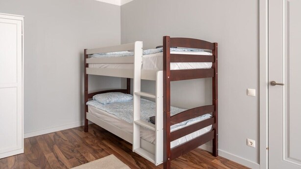 A bunk bed with three levels, white bedding, and a wooden frame. - Spacious Family Haven in Riga’s Historic Heart (Rīga)