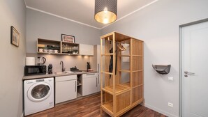 A compact kitchen with a washing machine, microwave, and wooden shelving unit. - Spacious Family Haven in Riga’s Historic Heart (Rīga)