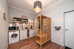 A compact kitchen with a washing machine, microwave, and wooden shelving unit. - Spacious Family Haven in Riga’s Historic Heart (Rīga)