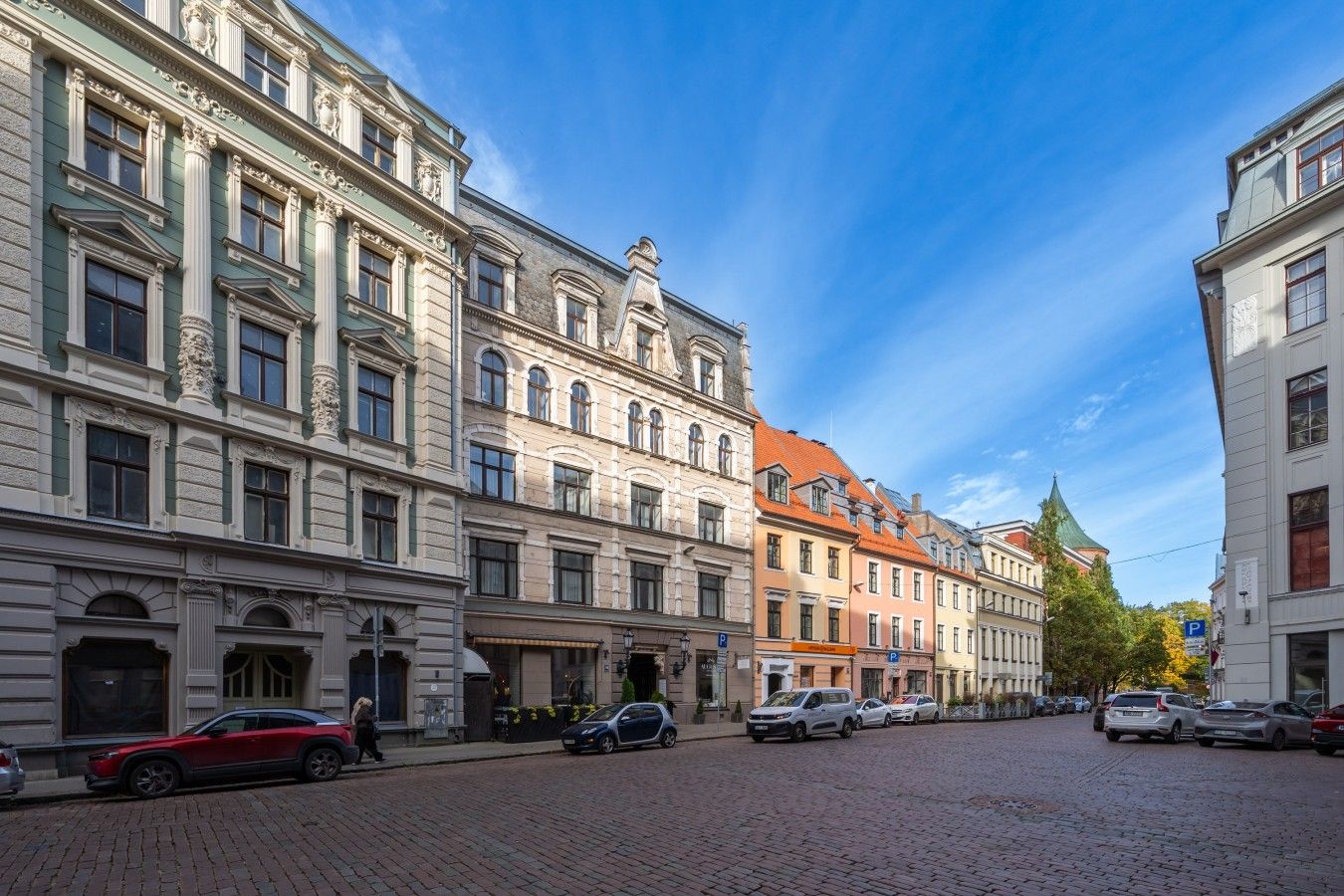 Une rue pavée bordée de bâtiments historiques à l’architecture classique, sous un ciel d’un bleu éclatant.