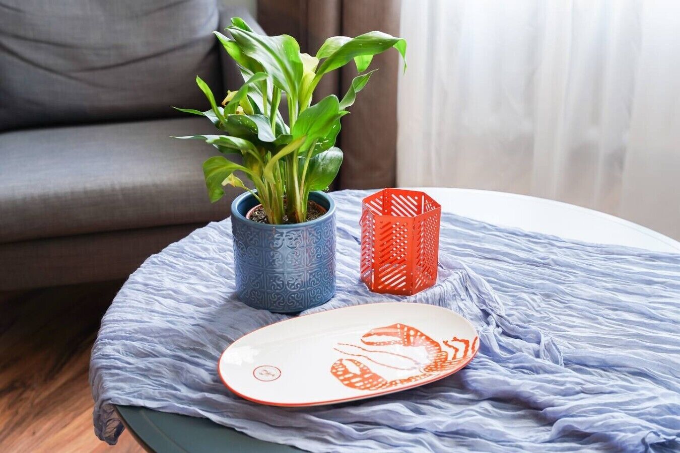 Une table ronde recouverte d’une nappe bleue, un pot de fleurs et un panier rouge.