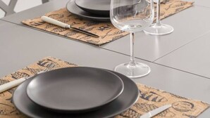 A table set with black plates, white cutlery, and clear wine glasses on a patterned placemat. - Spacious Family Haven in Riga’s Historic Heart (Rīga)