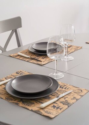 A table set with black plates, white cutlery, and clear wine glasses on a patterned placemat. - Spacious Family Haven in Riga’s Historic Heart (Rīga)