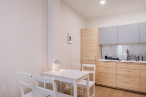 A modern kitchen with white cabinets, a white table, and chairs. - Artilerijas 1-bedroom apartment | Courtyard View (Riga)