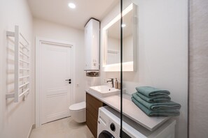 A modern bathroom with a toilet, sink, and washing machine. - Artilerijas 1-bedroom apartment | Courtyard View (Riga)
