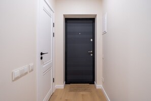 A hallway with a black door, white walls, and a wooden floor. - Artilerijas 1-bedroom apartment | Courtyard View (Riga)
