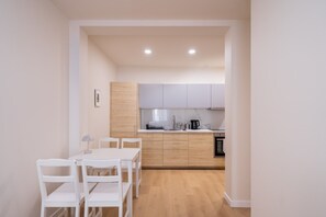A compact kitchen with white cabinets, a dining table with chairs, and a small oven. - Artilerijas 1-bedroom apartment | Courtyard View (Riga)