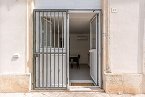An open metal gate leading to a room with a table and chairs, a doormat, and a wall-mounted air conditioning unit. - Dinologo Modern Flat by Wonderful Italy (Syracuse)