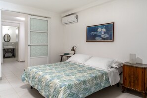 A bedroom with a bed, a bedside table, a nightstand, a painting, and an air conditioning unit. - Dinologo Modern Flat by Wonderful Italy (Syracuse)