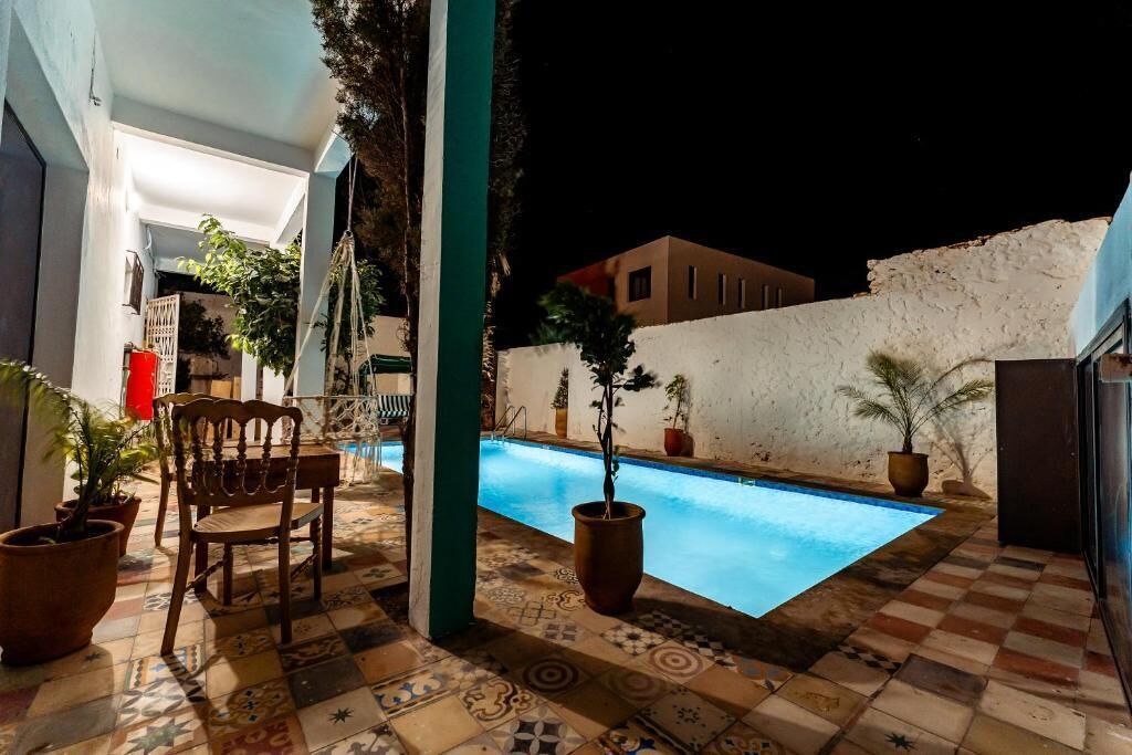 A pool area with a tiled floor, a wooden chair, and potted plants.