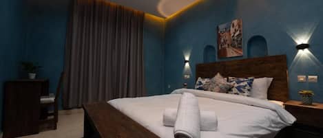 A bedroom with a large bed, a wooden bench, a desk, and a chair.