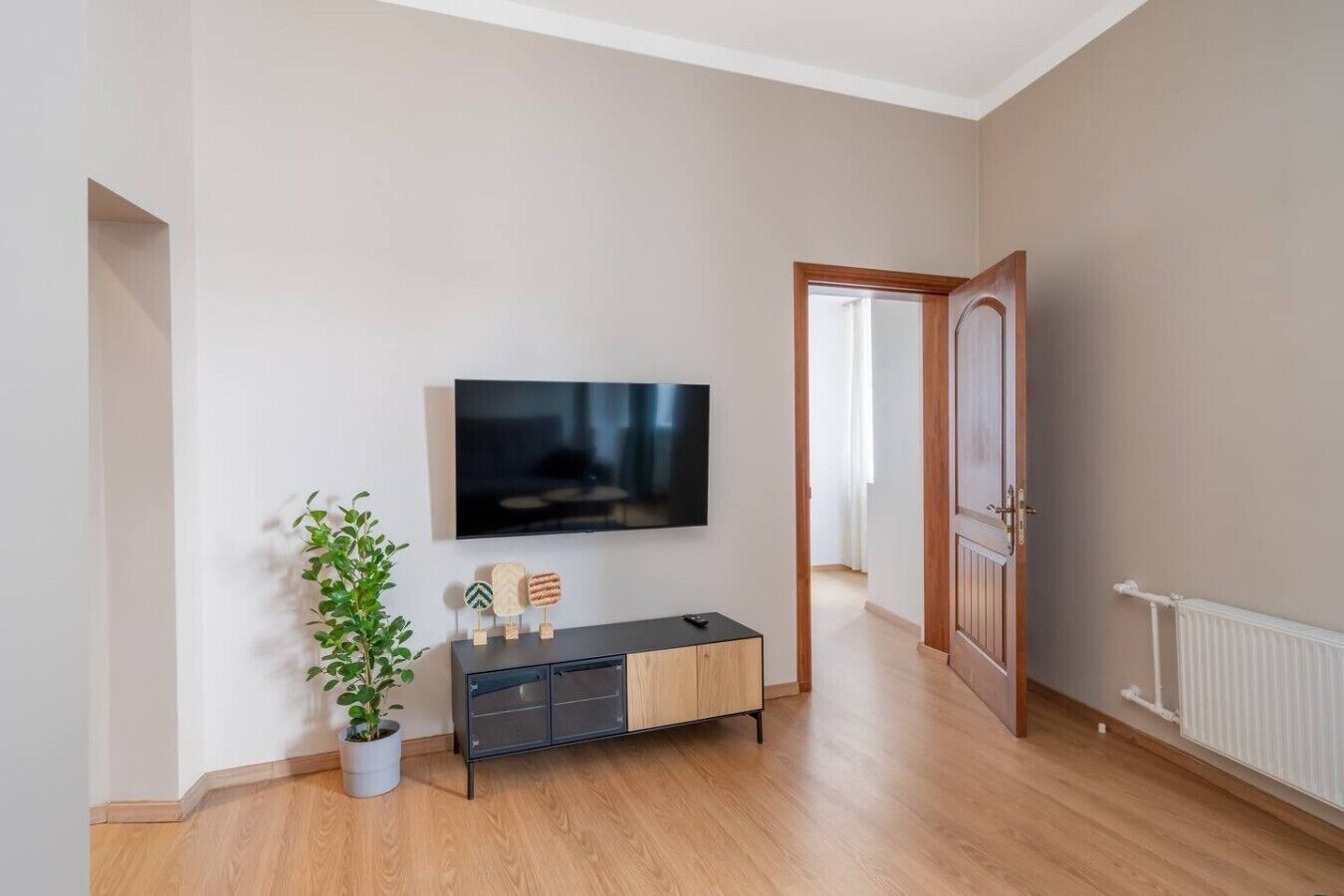 A modern living room with a flat-screen TV mounted on the wall, a wooden floor, a potted plant, and a minimalist console table.