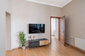 A modern living room with a flat-screen TV mounted on the wall, a wooden floor, a potted plant, and a minimalist console table. - Heart of Old Town TOP location 1-Bedroom Apartment (Riga)