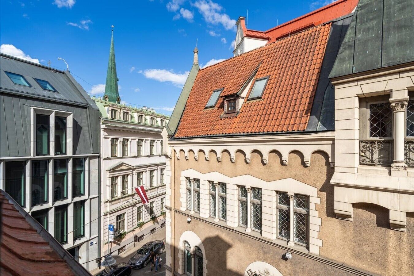 Vista de una calle con edificios de arquitectura tradicional, incluyendo una aguja de iglesia y un edificio con tejado de tejas rojas.