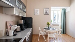 Eine kleine Küche mit modernen Geräten, ein Essbereich mit Tisch und Stühlen sowie ein Fenster mit Vorhängen.
