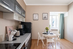 A compact kitchen with modern appliances, a dining area with a table and chairs, and a window with curtains. - Heart of Old Town TOP location 1-Bedroom Apartment (Riga)
